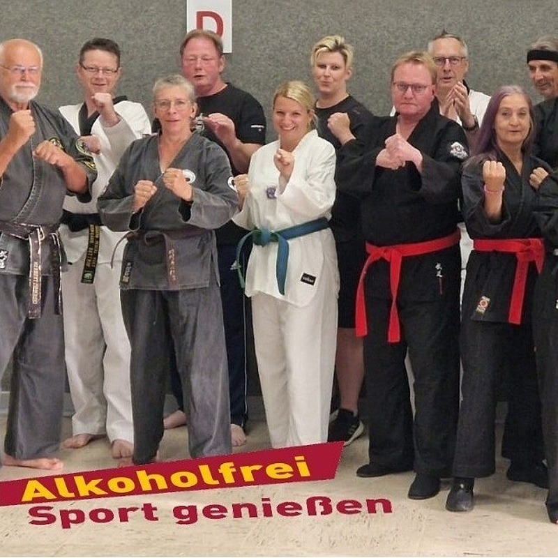 Kampfsportlerinnen und Kampfsportler der Jutsu-Akademie-Harms vor dem Logo "Alkoholfrei Sport genießen" in Kampfstellung
